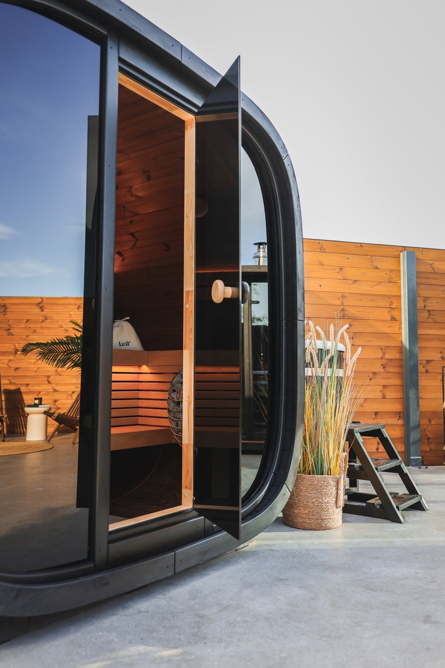 Modern Leil Black Cube Classic outdoor sauna featuring Thermowood construction, alder wood interior benches, smoked glass facade, and LED lighting